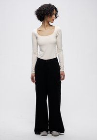 Dugi rukav, kremasti gornji dio s kvadratnim izrezom uparan s širokim crnim cargo hlačama s kopčanjem na gumbe i džepovima. Ravne cipele.