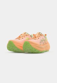 Running shoes featuring a mesh upper in peach and cream with green rubber soles, textured tread, and contrast orange laces.