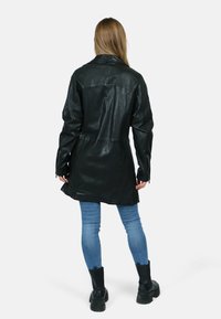 Svart läderjacka med avslappnad passform, långa ärmar, midjelång design och dragkedjedetaljer. Bärs över blå jeans och svarta ankelstövlar.