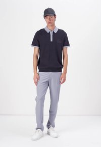 Polo azul marinho com gola e punhos cinza claro, design de tecido texturizado. Combinado com calças cinza claro e ténis brancos. Boné escuro.