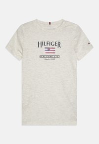 Svetle šedé tričko s krátkým rukávem vyrobené z měkké tkaniny, na kterém je ve středu nápis "HILFIGER" a grafický design americké vlajky.