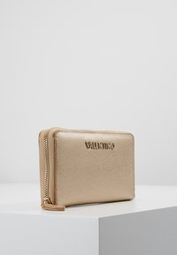 Gold textured wallet with a zip closure, featuring a raised logo on the front, rectangular shape, and smooth edges.