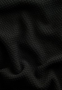 Gros plan sur un tissu en tricot gaufré noir avec un motif texturé en forme de grille et des plis doux.
