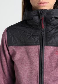 Ciemnoszara i burgundowa kurtka z pikowanym górnym odcinkiem, wysokim kołnierzem i zapięciem na zamek. Posiada teksturowany materiał i kontrastujące kolory.