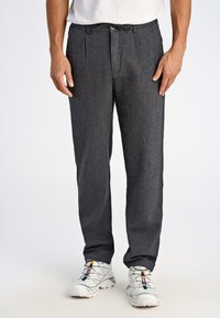 Pantaloni a righe grigie realizzati in tessuto leggero, con una vestibilità comoda, chiusura con cordoncino e tasche laterali. Abbinati a scarpe da ginnastica bianche.