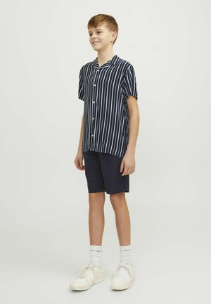 Marinblå randig kortärmad skjorta med knappar, matchad med mörka shorts, vita sneakers och vita strumpor. En enkel, avslappnad klädsel för ungdomar.
