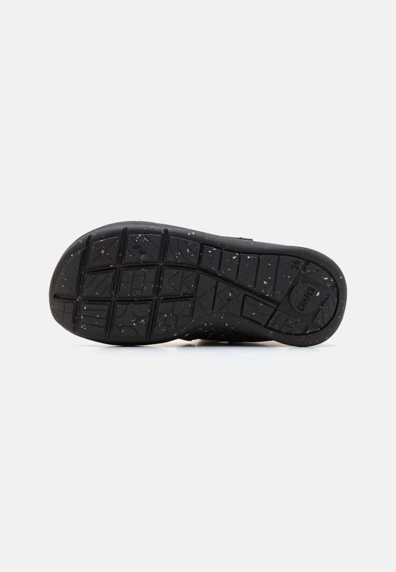 Suola di scarpa nera con motivo di battistrada testurizzato e piccole macchie bianche. Presenta un bordo curvo e una sezione rialzata con il logo del marchio.
