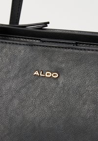 Schwarze Texturierte Kunstledertasche mit einem goldenen "ALDO"-Logoanhänger, klaren Linien und einem eleganten Design.