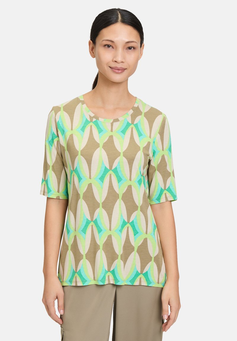 Short-sleeved blouse in a tan fabric with a geometric pattern in green, teal, and cream. Features a round neckline and relaxed fit.