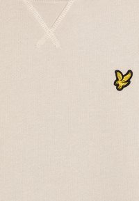 Maglione beige con lavorazione a maglia testurizzata, caratterizzato da un collo a V e un logo di un uccello ricamato in nero e giallo sul lato sinistro del petto.