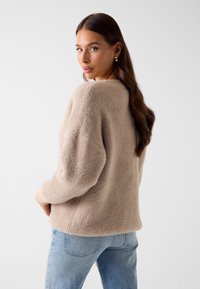 Beige gebreide trui met een gestructureerde afwerking, een losse pasvorm en verlaagde schouders. Gecombineerd met lichtblauwe jeans. Zachte en gezellige uitstraling.