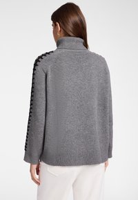 Szary dzianinowy sweter z wysokim kołnierzem, ozdobiony czarnymi sznurowaniami wzdłuż ramion oraz ściągaczami przy mankietach. Miękka tekstura i swobodny krój.