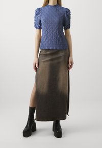 Modrá texturovaná blůza s nafouknutými rukávy, v kombinaci s hnědou, sukní ke kolenům s bočním rozparkem. Černé silné platformové boty dotvářejí celý vzhled.