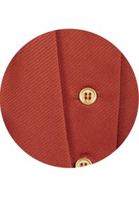 Rostfärgad stickad tyg med en texturerad yta, prydd med en gul knapp. Tyget har diagonal ribbning och en slät finish.