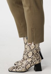 Bruine broek met ritssluiting en beige enkellaarsjes met slangenprint en een stevige zwarte hak. Gestructureerde materialen, een getailleerde pasvorm en opvallende patronen.