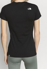 Černé bavlněné tričko s krátkými rukávy, s malým bílým logem na horní části zad a štítkem na lemu u pasu.