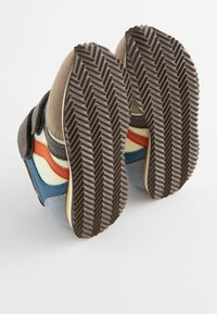 Baskets avec une semelle en caoutchouc texturé marron, une tige en suède et tissu, arborant des rayures multicolores en rouge, bleu, crème et gris.
