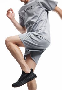 Grå atletisk t-shirt med teksten "FREMTID", parret med grå shorts med neon detaljer. Personen bærer sorte slip-on sneakers.