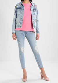 Veste en jean avec broderies florales, chemise en coton rose, jean skinny bleu clair déchiré avec des embellissements, et talons roses clairs.