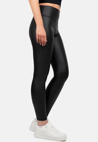 Leggings neri a vita alta realizzati in un materiale lucido, con una texture liscia e una silhuette aderente. Indossati con sneakers bianche.