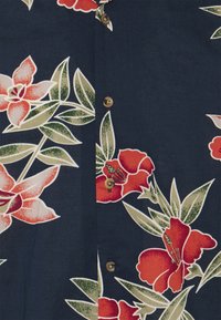 Ciemnoniebieska tkanina z czerwonymi i pomarańczowymi tropikalnymi kwiatami oraz zielonymi liśćmi, z brązowymi guzikami w pionowym rzędzie.