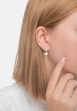Orecchini a perno a forma di cuore in oro con un dettaglio in perla pendente. Il design è elegante, con una finitura lucida e una texture liscia.
