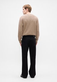 Bežinis tekstūruotas megztinis derinamas su juodomis plačiomis džinsomis. Apranga pasižymi paprastu dizainu ir ją papildo juodi bateliai.