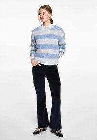 Prúhovaný sveter v modrej a sivej farbe, s voľným strihom, kombinovaný s čiernymi rozšírenými cargo nohavicami. Obuv tvoria čierne balerínky s mašľami.