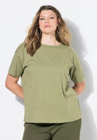 Oliwkowozielony t-shirt z krótkim rękawem i okrągłym dekoltem, ozdobiony rozproszonymi złotymi gwiazdkami, w połączeniu z teksturowanymi zielonymi spodniami.