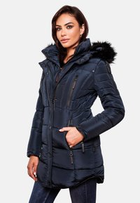 Marinblå vadderad parka med fuskpälsfodrad huva, dragkedjefickor och knappstängning. Har en något böjd nederkant och quiltad textur.