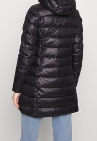 Sort pufferjakke med hætte, med et quiltet design, blank overflade og en halvlang silhuet, parret med blå jeans.