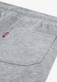 Shorts en coton gris avec une taille élastique, dotés d'une poche appliquée et d'une petite étiquette rouge sur le côté. La texture de la surface est douce.