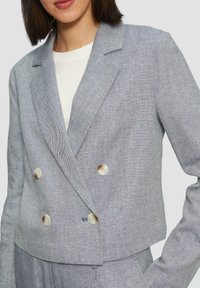 Dubbelbreasted blazer in een lichtblauw visgraatpatroon. Beschikt over grote ronde knopen en heeft een cropped pasvorm met gestructureerde schouders.