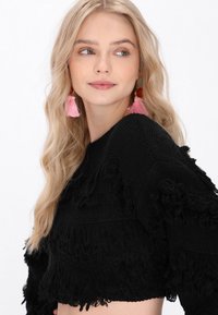 Maglione corto nero con dettagli in frange testurizzate, tessuto lavorato a maglia, scollatura rotonda e maniche lunghe. Orecchini a nappina rosa che aggiungono colore.