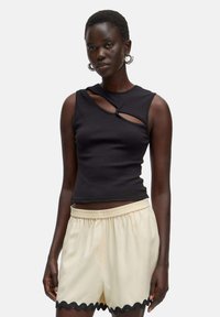 Zwarte geribbelde tanktop met uitsnijding aan de voorkant, gecombineerd met crème shorts met een gegolfde zoom en een elastische tailleband.