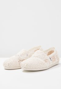 Chaussures à enfiler en dentelle écrue avec motifs floraux, tissu doux, bout arrondi, empiècements élastiques sur les côtés et semelle légère pour le confort.