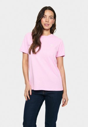 Pink cotton t-shirt with short sleeves, round neckline, and a small bow logo on the left chest. Paired with dark blue jeans.