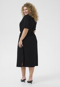 Black knee-length dress in a soft, textured fabric, featuring short sleeves, a belted waist, and side slit accents.