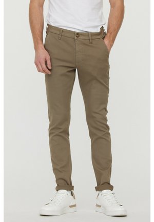 Pantalons slim-fit en khaki fabriqués en mélange de coton, dotés d'une fermeture à bouton, de cinq poches et de poignets retroussés, associés à des baskets blanches.