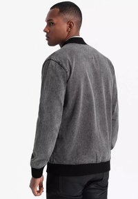 Giubbotto in denim grigio con colletto e polsini neri a coste, caratterizzato da una vestibilità comoda e un design minimale, visto di spalle.
