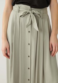 Jupe plissée vert clair avec une taille à nouer, dotée d'une fermeture à boutons à l'avant et d'une texture de tissu douce et lisse.
