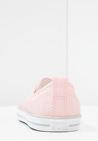 Zapatilla Converse All Star baja color rosa claro vista desde atrás, mostrando los detalles de costura y la suela de goma blanca con el logo.