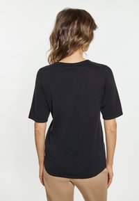 Sort kortærmet top med rund halsudskæring, ribbet tekstur og rund kant. Bæret med beige bukser.