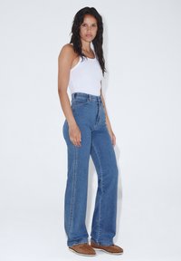 Jeans blu a vita alta in denim, con un design a gamba svasata. Abbinati a un top bianco senza maniche e mocassini marroni.