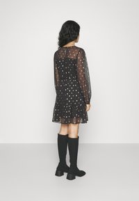 Μαύρο φόρεμα με πουά σχέδιο, διαφανή μανίκια και λεπτομέρεια με φροντίδα στο τελείωμα. Φοριέται με μαύρες μπότες μέχρι το γόνατο. Η πίσω πλευρά έχει άνοιγμα σε σχήμα κλειδαριάς.