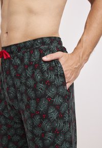 Svarta loungebyxor med ett mönster av gröna tallnålar och röda bär, med resårmidja och röd dragsko, samt sidofickor.