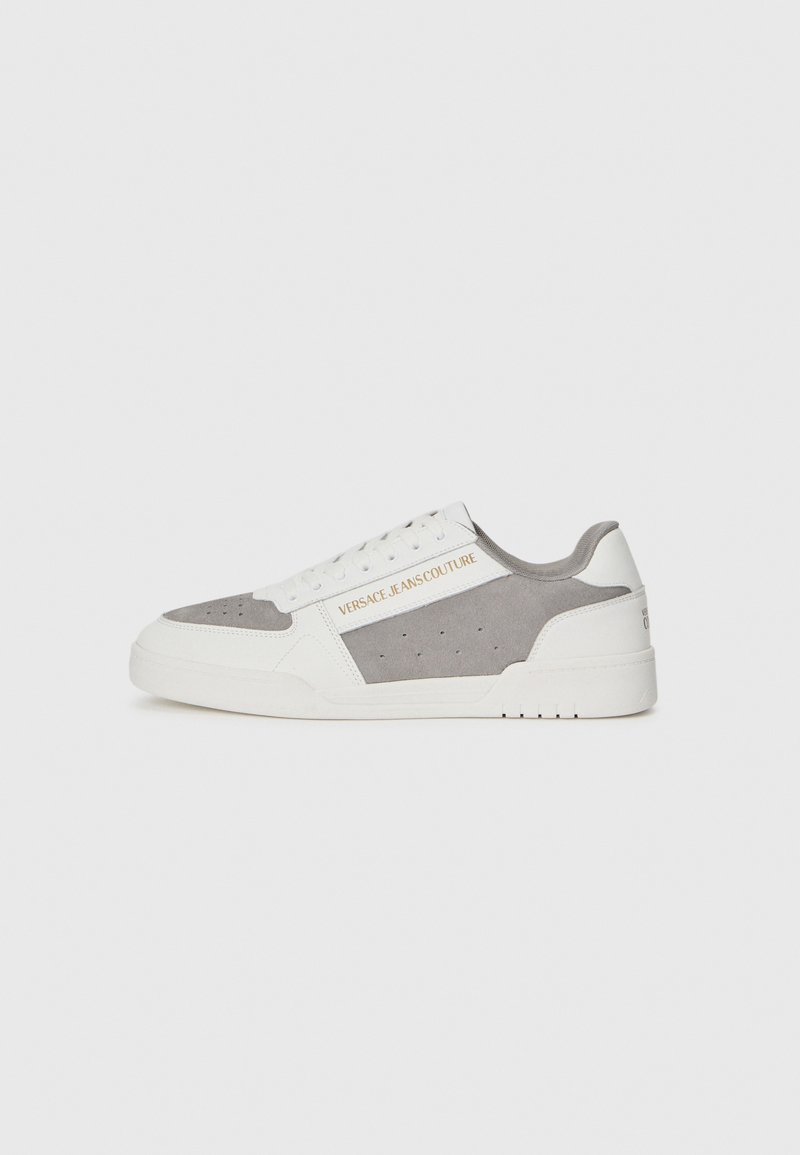 Ténis Versace Jeans Couture em branco e cinza, apresentando uma mistura de couro e camurça, textura perfurada e uma marcação visível na lateral.