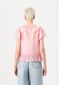 Top rosa, semi-trasparente con colletto e maniche arricciate, caratterizzato da un orlo arricciato. Il design sul retro è semplice con una vestibilità rilassata.
