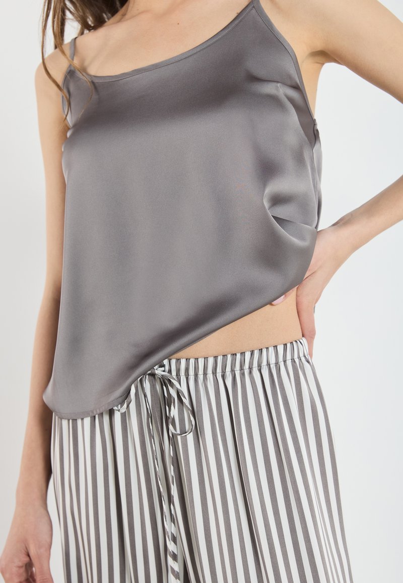 Camisole en satin gris avec bretelles réglables, associé à un pantalon à cordon de serrage rayé gris et blanc avec une taille élastique.