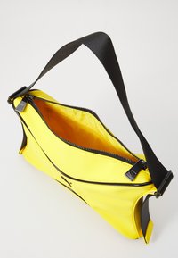 Gul syntetisk håndveske med svart stropp, med glidelås og oransje interiør. Glatt tekstur med buet design.